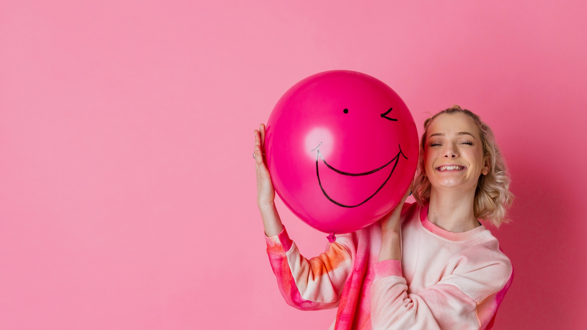 Smiling woman holding a bright pink balloon against a pink background
