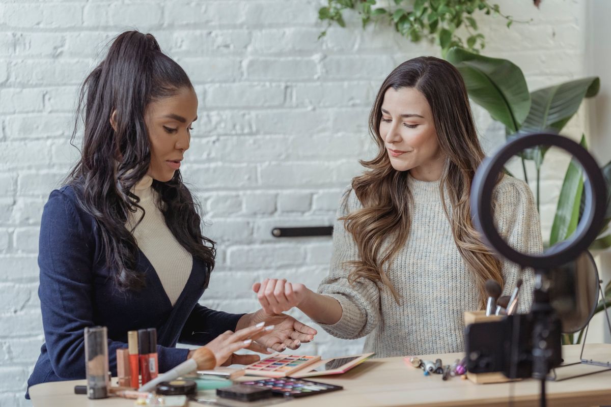 Two beauty creators filming a makeup tutorial with products and a ring light